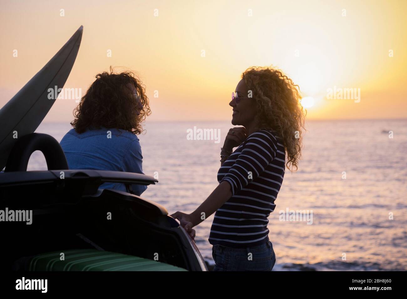 Coppia di donne di bellezza in vacanza godere l'amicizia di fronte a un tramonto colured con orizzonte oceano - viaggio e stile di vita concetto per i giovani - capelli ricci e immagine di libertà Foto Stock