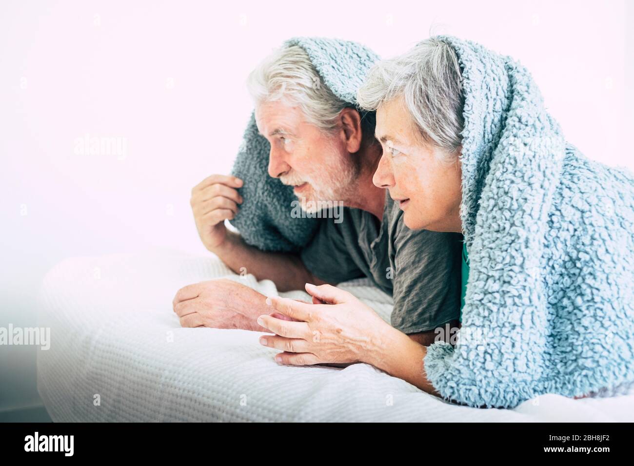 Giocoso matura coppia caucasica a homer giocando sotto il coperchio sul letto in camera da letto - bianco brillante concetto di immagine con persone di età Foto Stock
