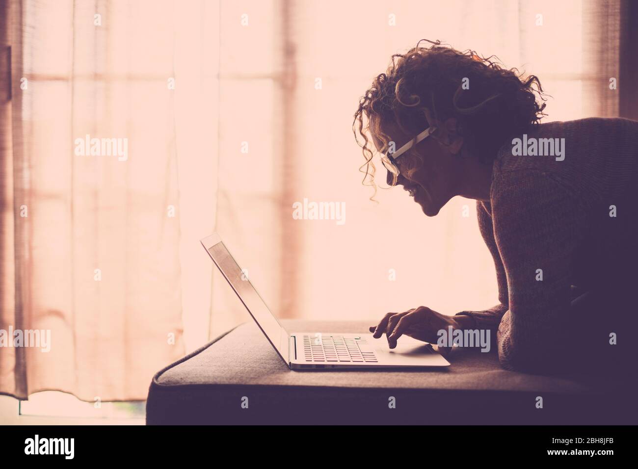 donna con capelli ricci e occhiali che lavora con computer portatile comodamente seduto sul divano a casa. Concetto di indipendenza della tecnologia per la signora di affari freelance - filtro caldo marrone Foto Stock