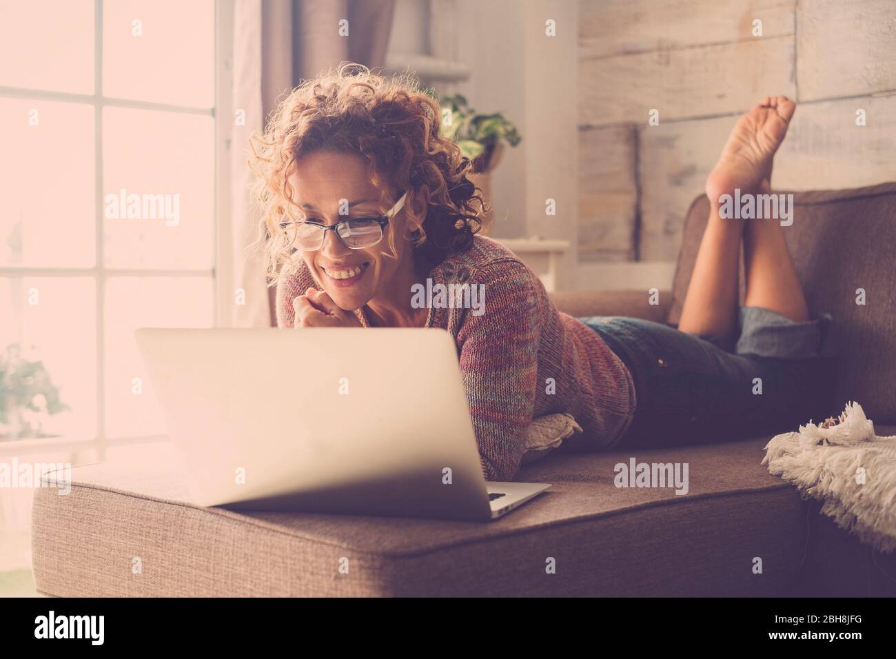 Donna sorridere e utilizzare un computer portatile collegato a Internet per guardare un film o lavorare facilmente a casa in un ufficio alternativo e stile di vita concetto - freelance e libera persone con tecnologia Foto Stock