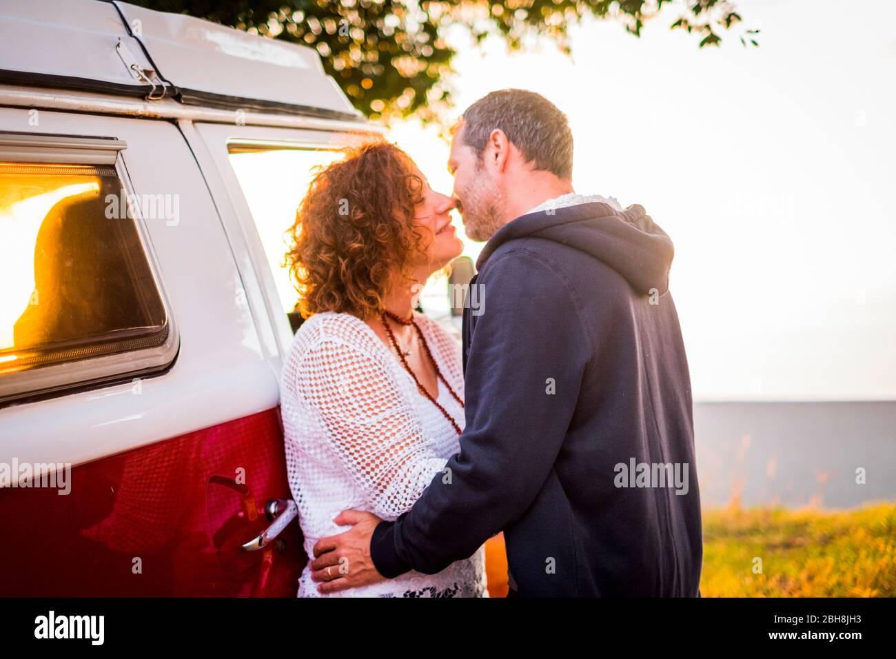 Giovane età media adulto uomo e donna baciare con amore all'aperto durante i viaggi vacanza - bus rosso in background e tempo al tramonto Foto Stock