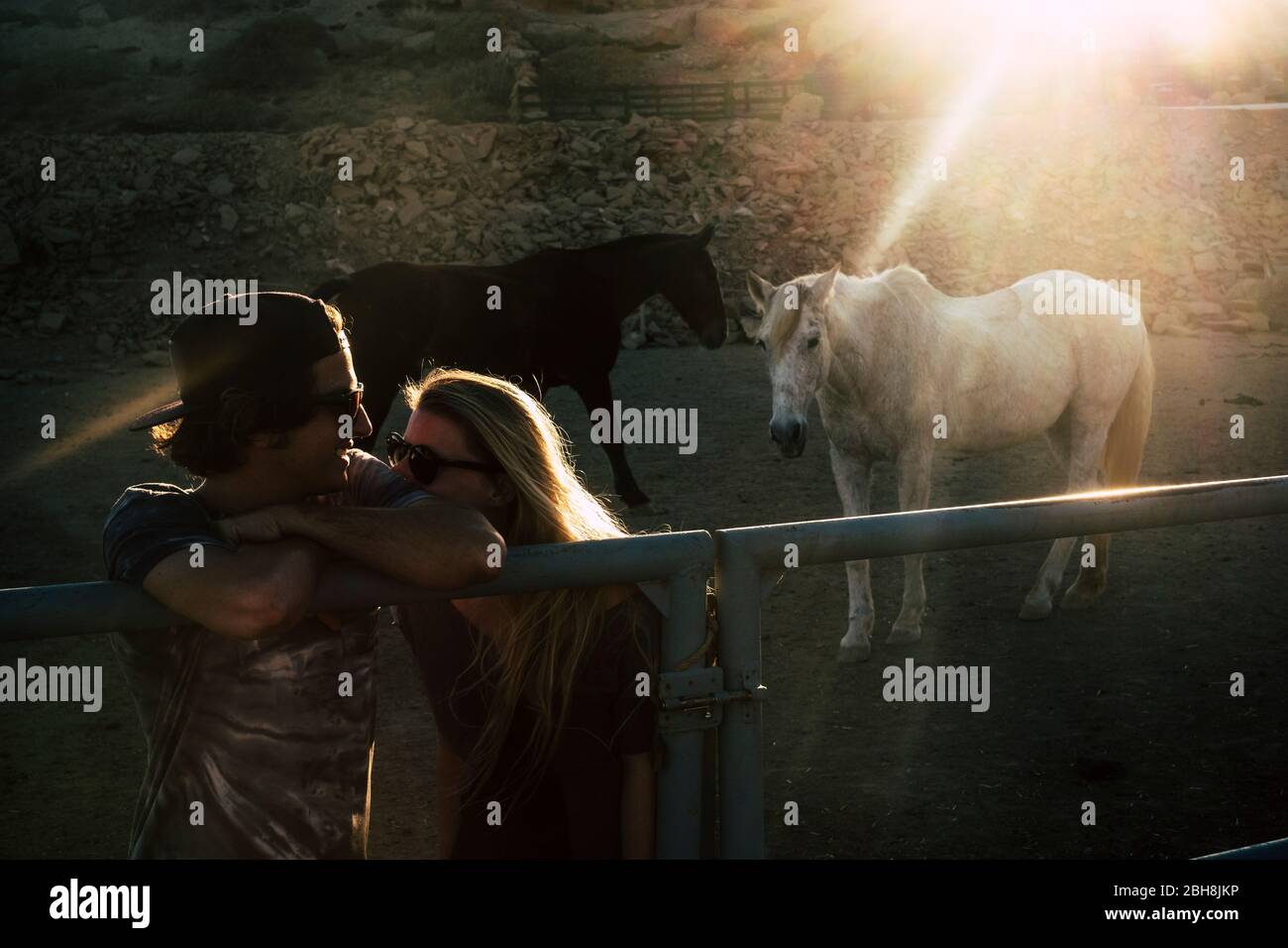 Luce romantica e coppia sussurrante insieme con amore durante il tramonto con due bellissimi cavalli sullo sfondo - romantico e concetto di relazione all'aperto con luce del sole Foto Stock