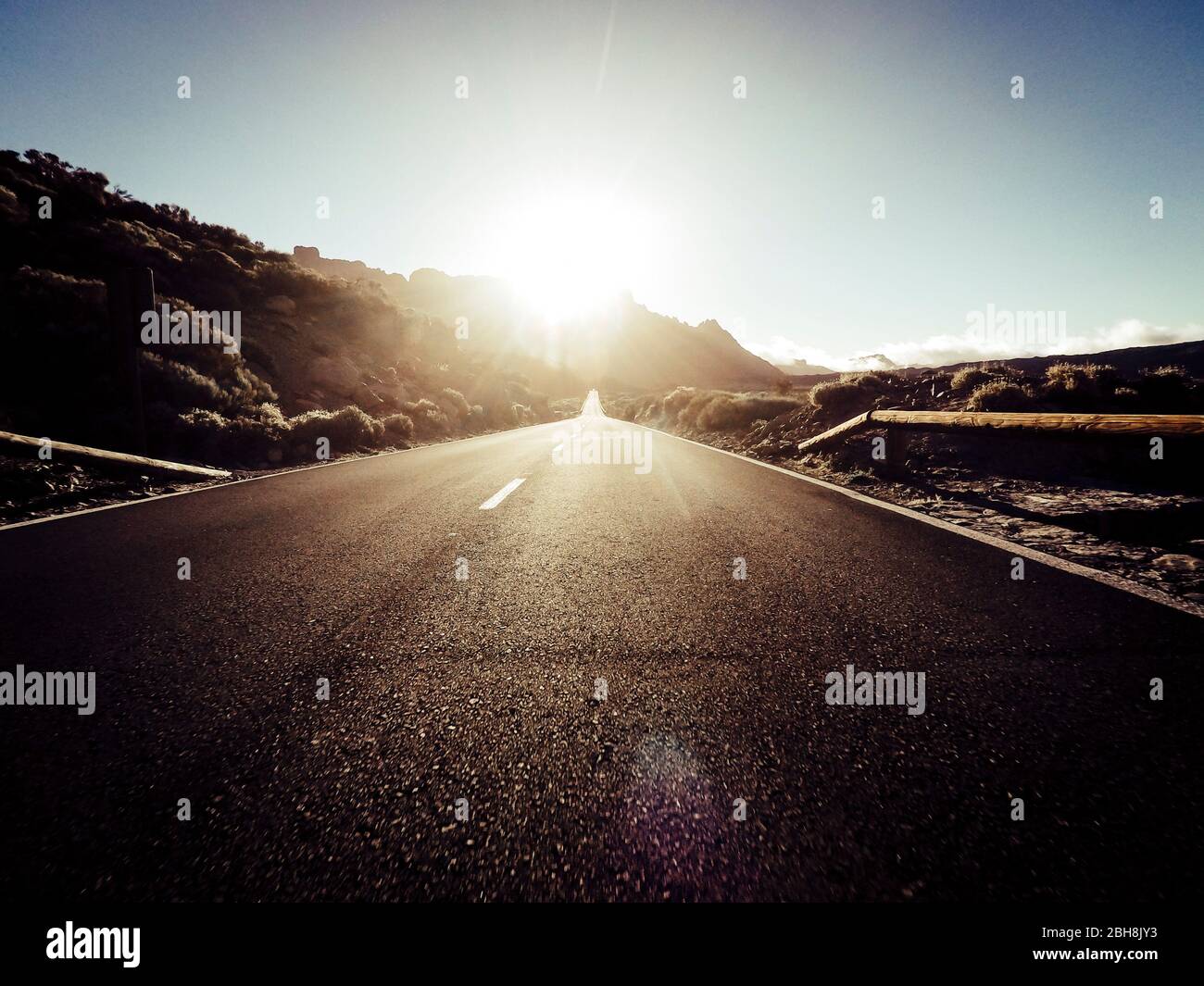 Strada lunga in montagna con sole davanti e luce del sole - punto di vista del terreno con asfalto nero e linee bianche - concetto di guida e viaggio Foto Stock