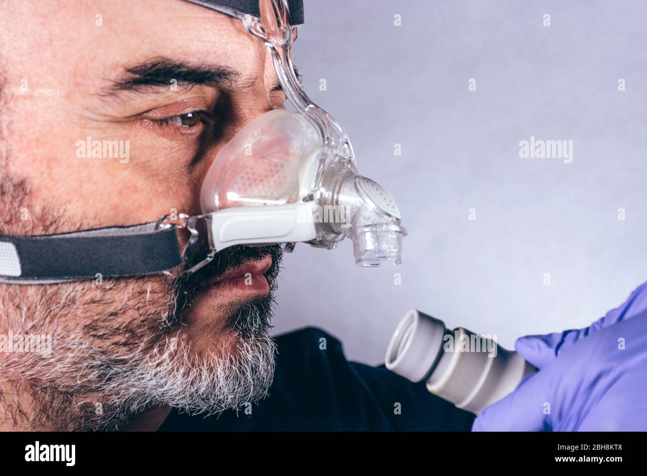 Mano con guanto medico mettendo su un uomo una maschera respiratoria per i disturbi del sonno. Sfondo bianco. Apnea. Dispositivi medici. Pompa dell'aria. Respirazione assistita Foto Stock