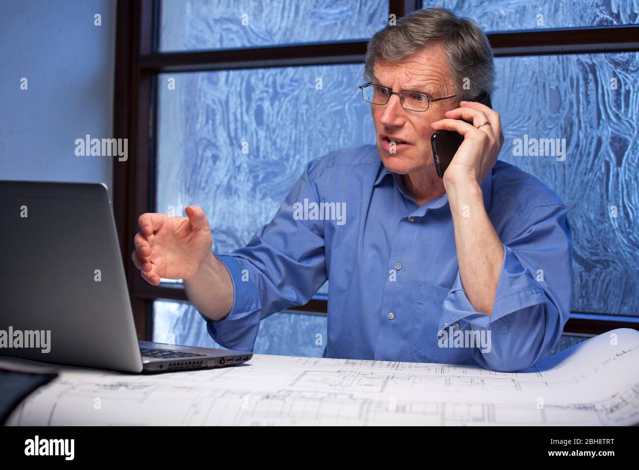 Uomo d'affari arrabbiato maturo che parla sul telefono cellulare e guarda il monitor di un notebook - concentrarsi sul viso Foto Stock