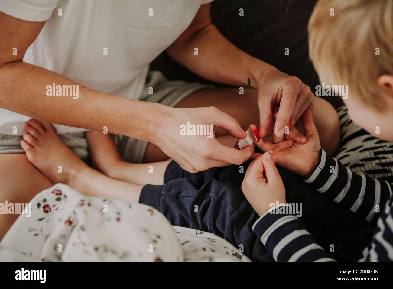 Morgens im Bett, Mutter verarztet Wunde am Finger ihres Sohnes Foto Stock