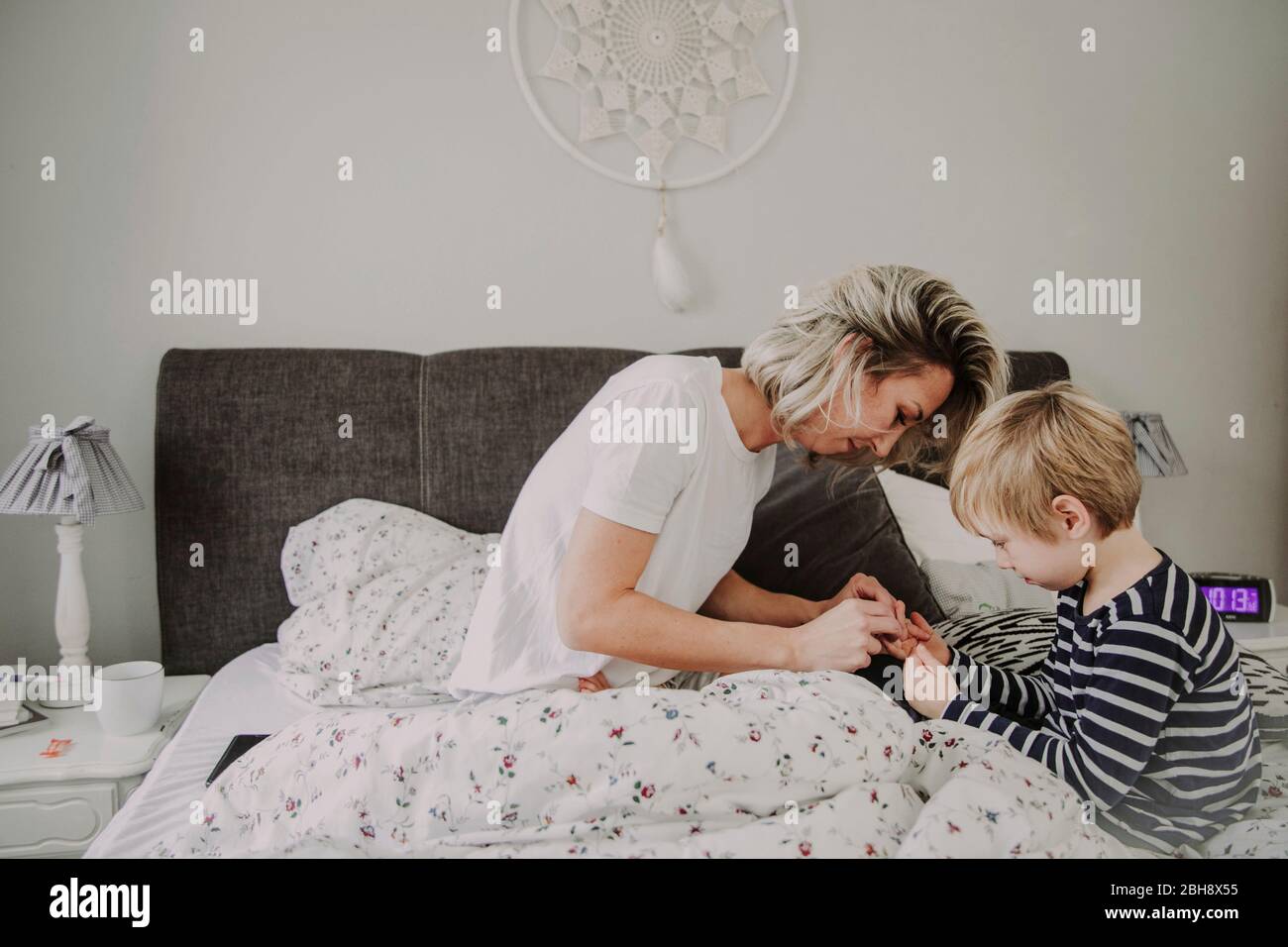 Morgens im Bett, Mutter verarztet Wunde am Finger ihres Sohnes Foto Stock