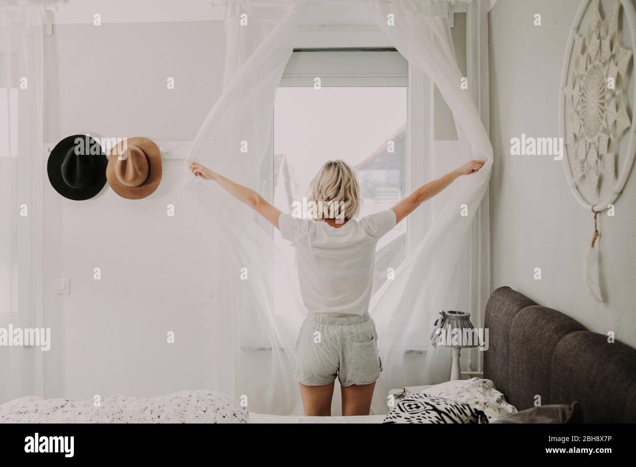 Frau steht am Schlafzimmerfenster und öffnet die Gardinen Foto stock - Alamy