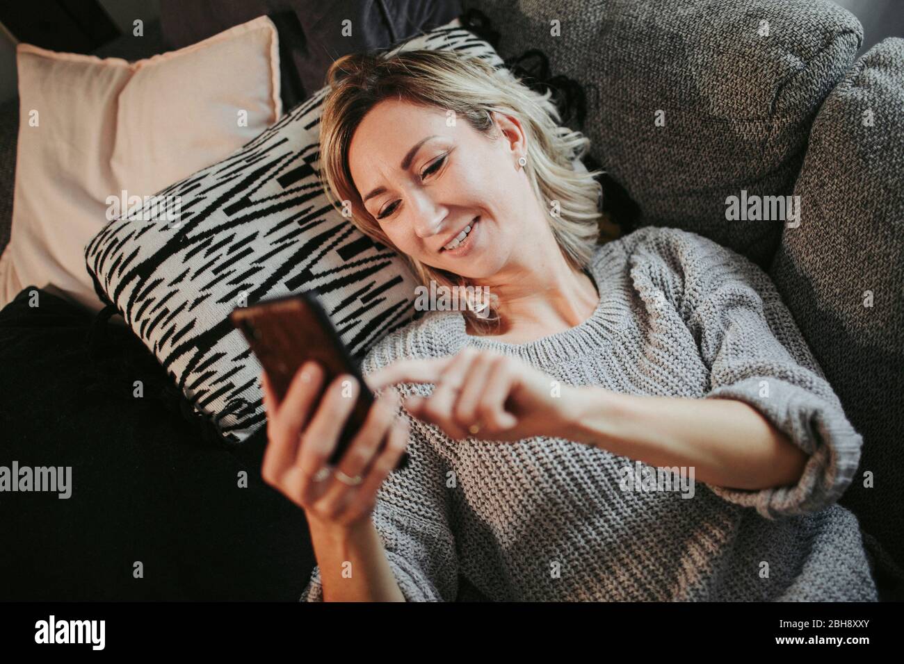 Frau liegt entspannt mit smartphone auf der Couch Foto Stock