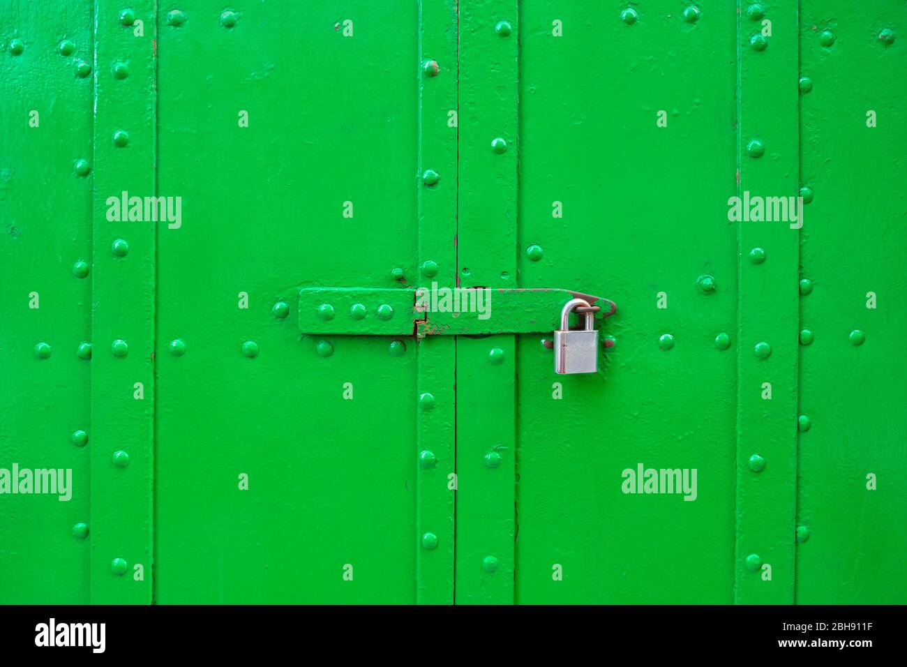 Porte in metallo verde vibrante con grandi rivetti, bloccate con un fermo e un lucchetto. Foto Stock