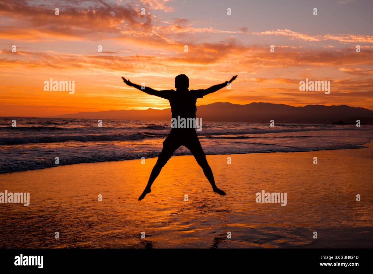 Silhouette di salto umano alto sulla spiaggia oceano. Tramonto serale Foto Stock
