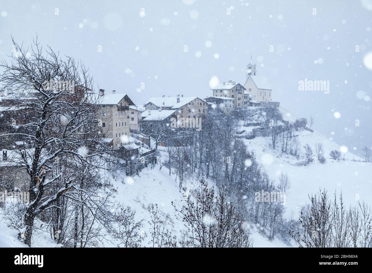 L'antico borgo di Colle Santa Lucia con la chiesa sulla collina sotto una nevicata, agordino, belluno, veneto, italia Foto Stock