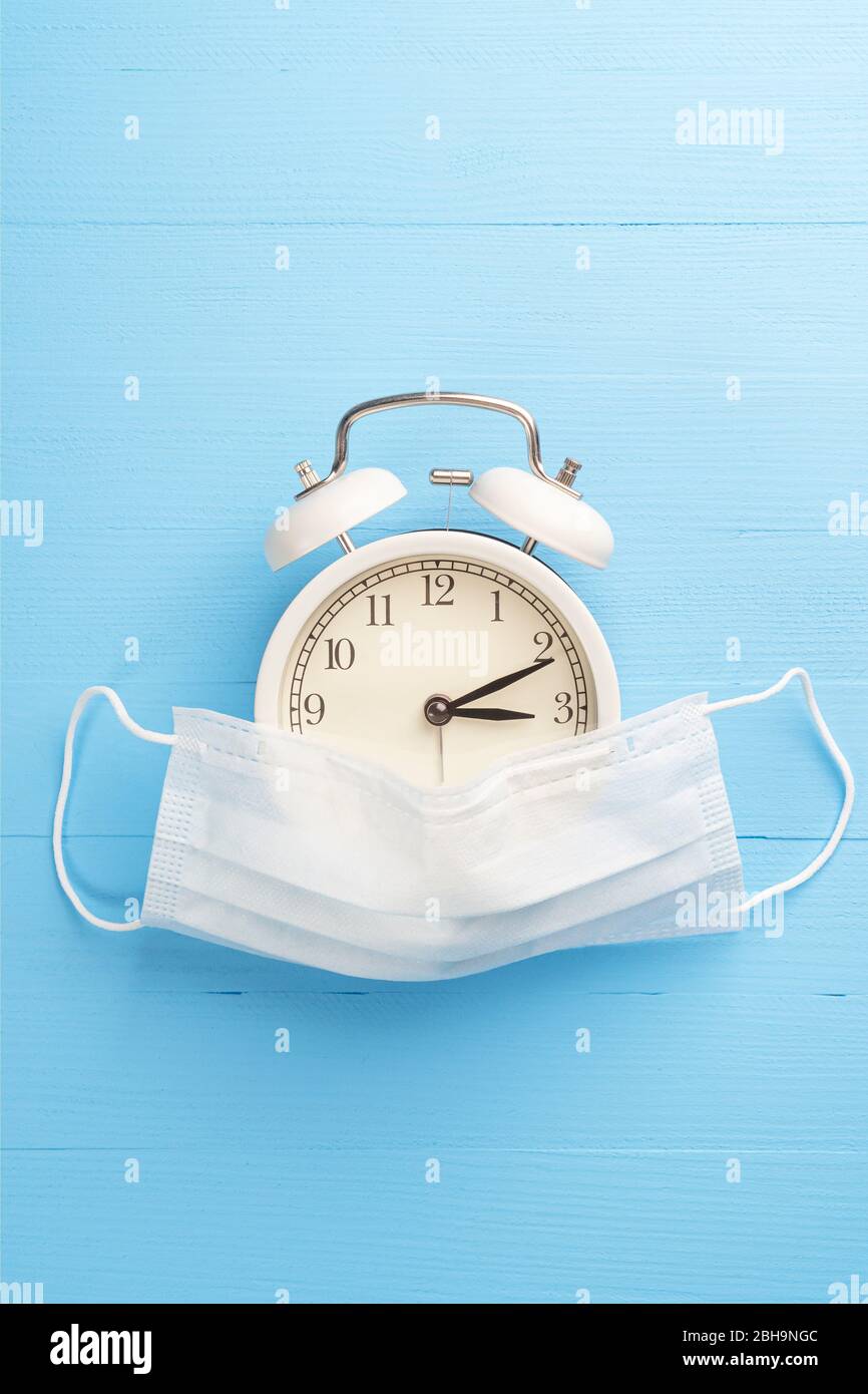 Maschera protettiva medica e sveglia su sfondo di legno blu e luminoso. Il concetto di misure preventive e di sicurezza contro l'infettio da coronavirus Foto Stock