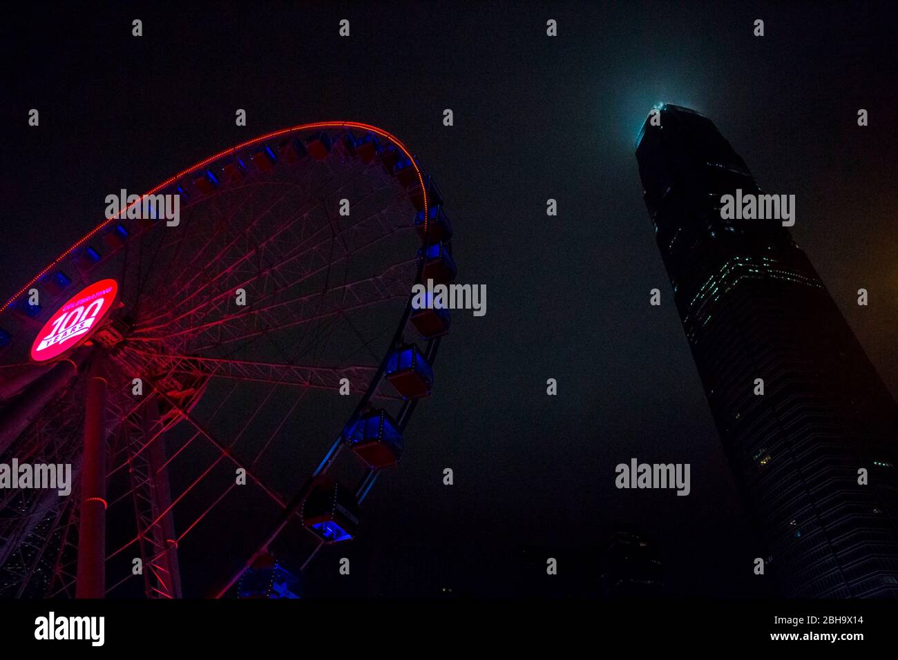 Ruota di ferro illuminata a luce rossa accanto al grattacielo di notte, porto, Hongkong Foto Stock