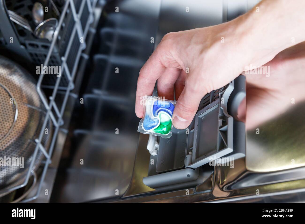 Primo piano della mano dell'uomo che mette la compressa in una scatola detergente per lavastoviglie, messa a fuoco morbida. Concetto di piatti sporchi. Foto Stock