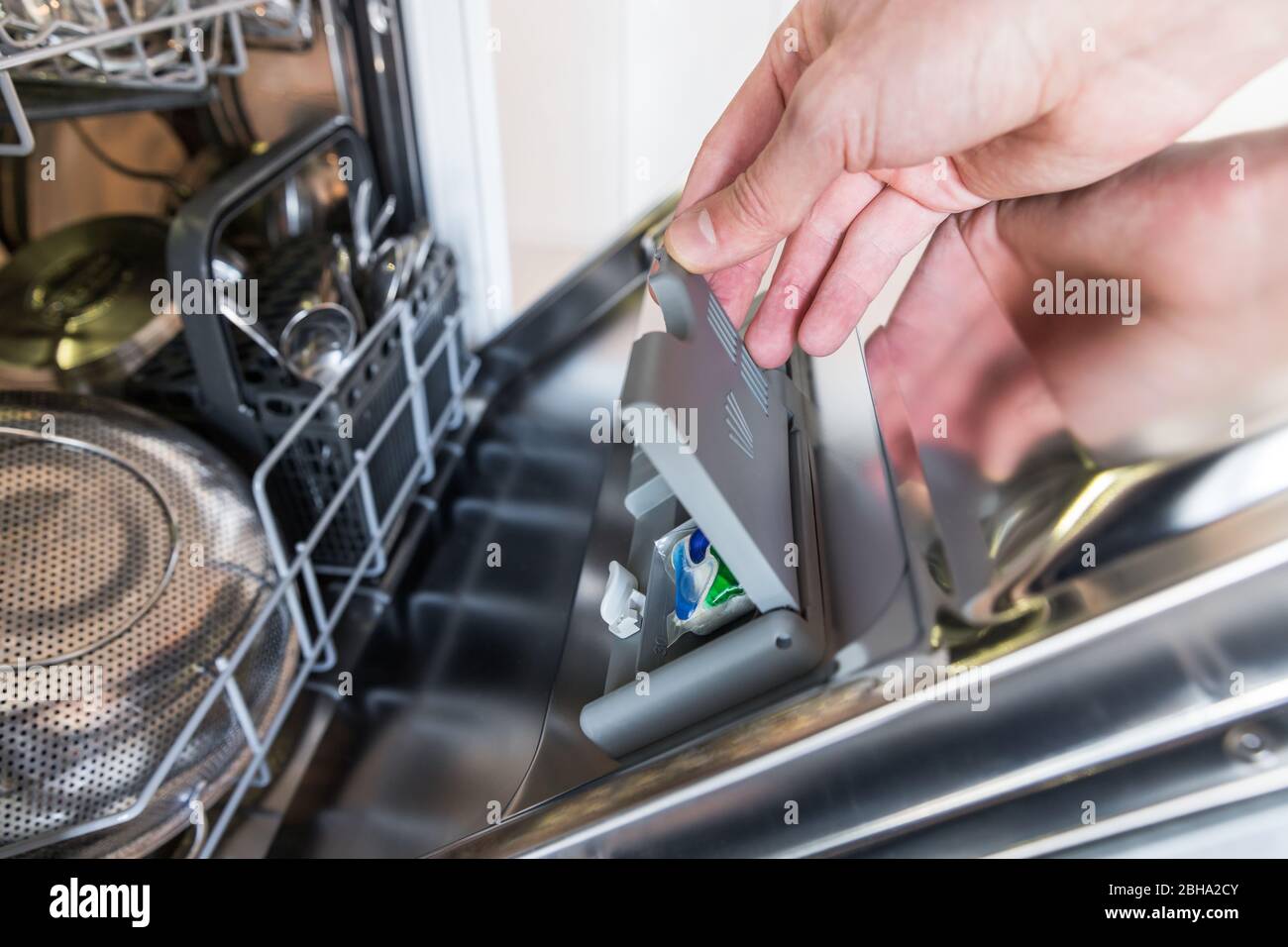 Primo piano della mano dell'uomo che mette la compressa in una scatola detergente per lavastoviglie, messa a fuoco morbida. Concetto di piatti sporchi. Foto Stock