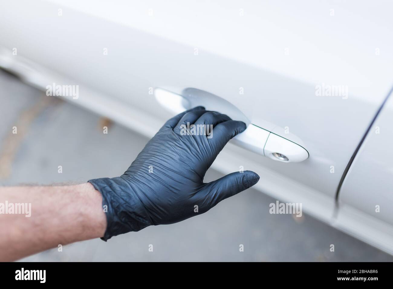 Indossare a mano guanti di gomma per uso medico che tengono la maniglia della porta dell'auto. Foto Stock