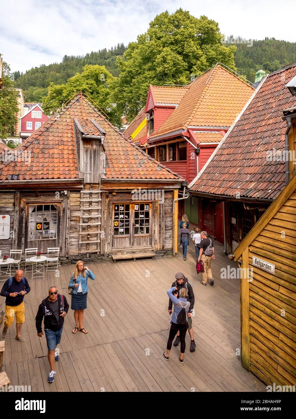 I turisti camminano su pannelli di legno in un romantico quartiere di case di legno con negozi e caffè con tavoli e sedie a Bryggen, Bergen, Bellgarden, Hordaland, Norvegia, Scandinavia, Europa Foto Stock