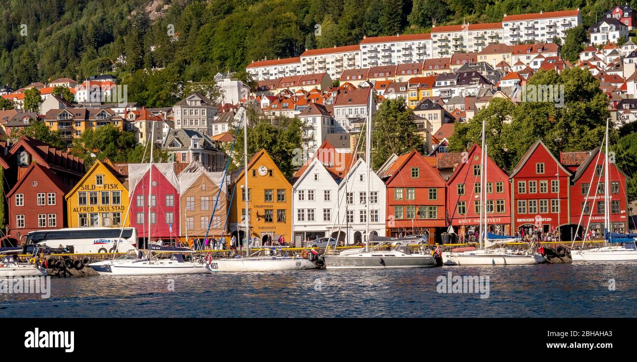 Nordsee, dietro una colorata case di legno fronte con barche a vela allegata nel porto di Bryggen, dietro di esso ulteriori case del posto sopra complessi alberghieri e foreste coperte di montagne, montagne, Hordaland, Norvegia, Scandinavia, Europa Foto Stock