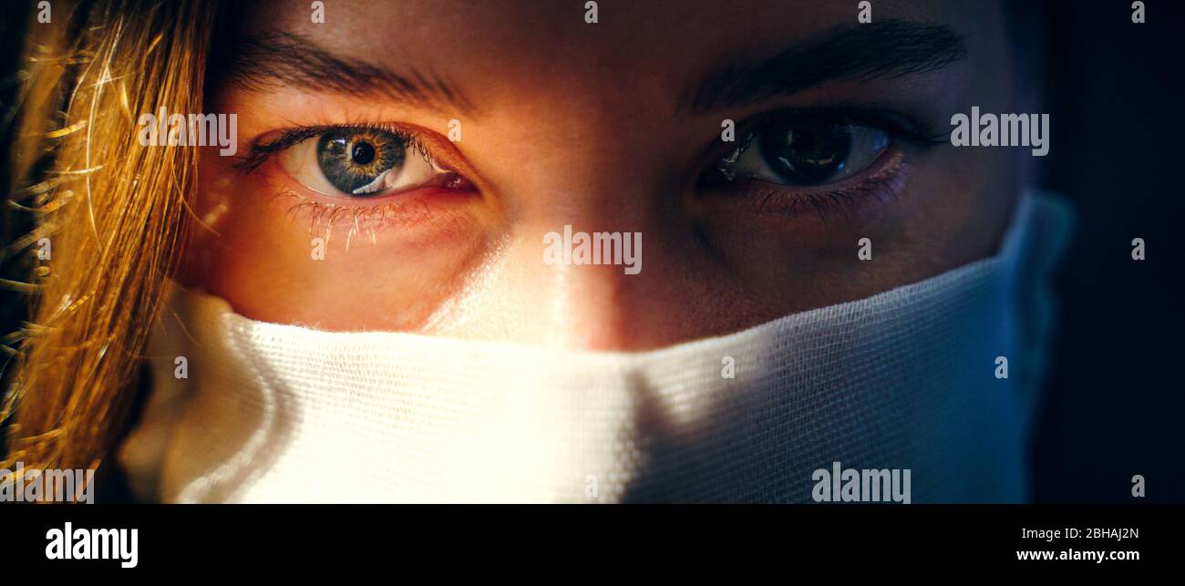 Occhi di una donna in una maschera di garza guardando la telecamera da vicino. Protezione preventiva della propria salute da infezioni virali. Concetto di coronavirus. Foto Stock