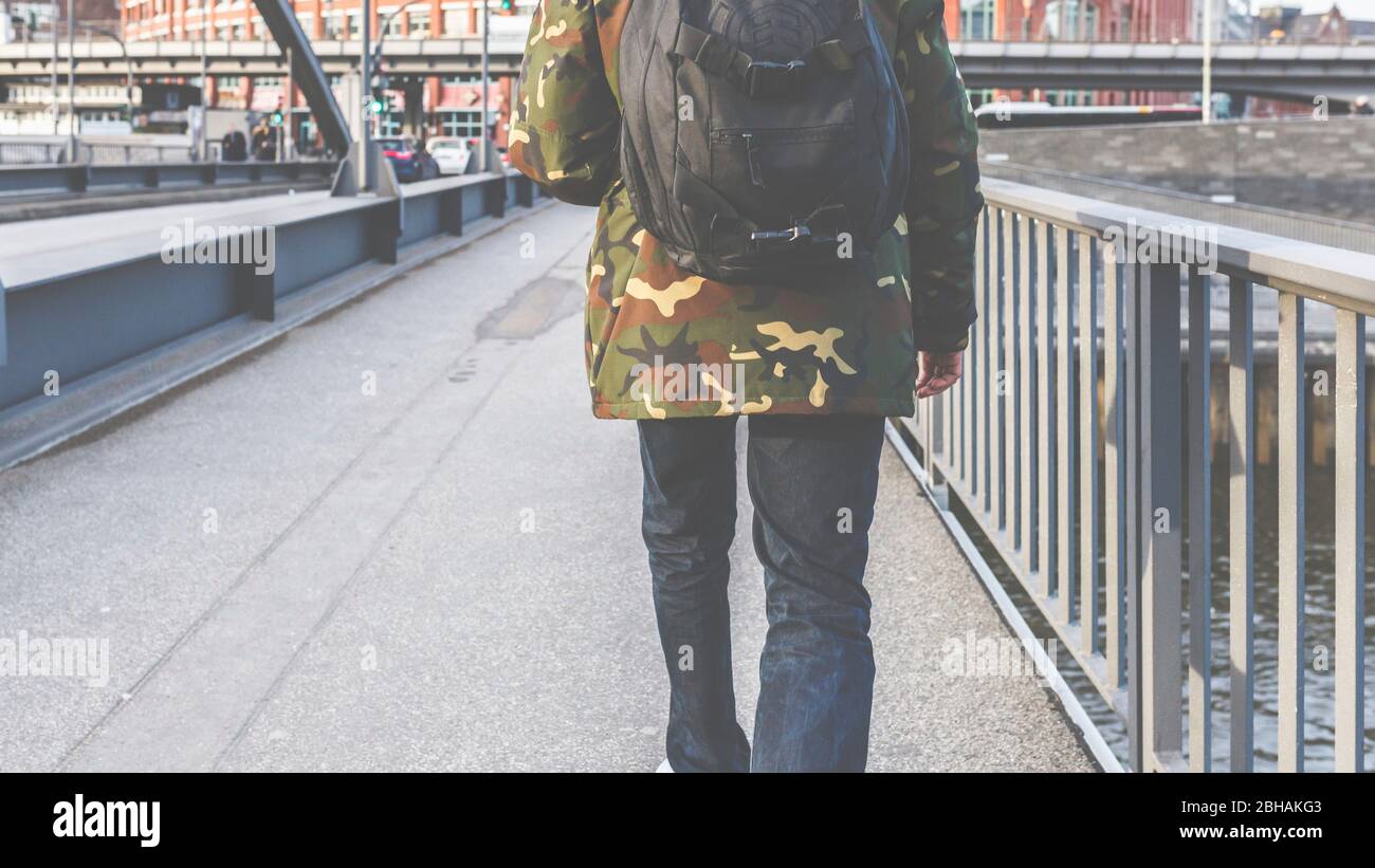 Un uomo in jeans e una giacca camuffata passa sopra un ponte di Amburgo. Foto Stock