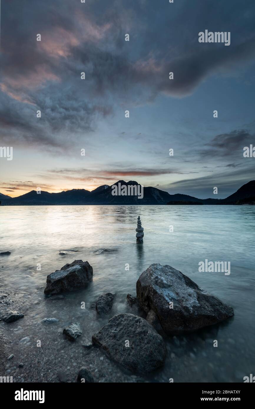 Pietre e sullo sfondo Steinmandl sulla riva di Walchensee durante il tramonto. Sullo sfondo le Prealpi bavaresi con l'Herzogstand, Heimgarten e Simetsberg. Foto Stock