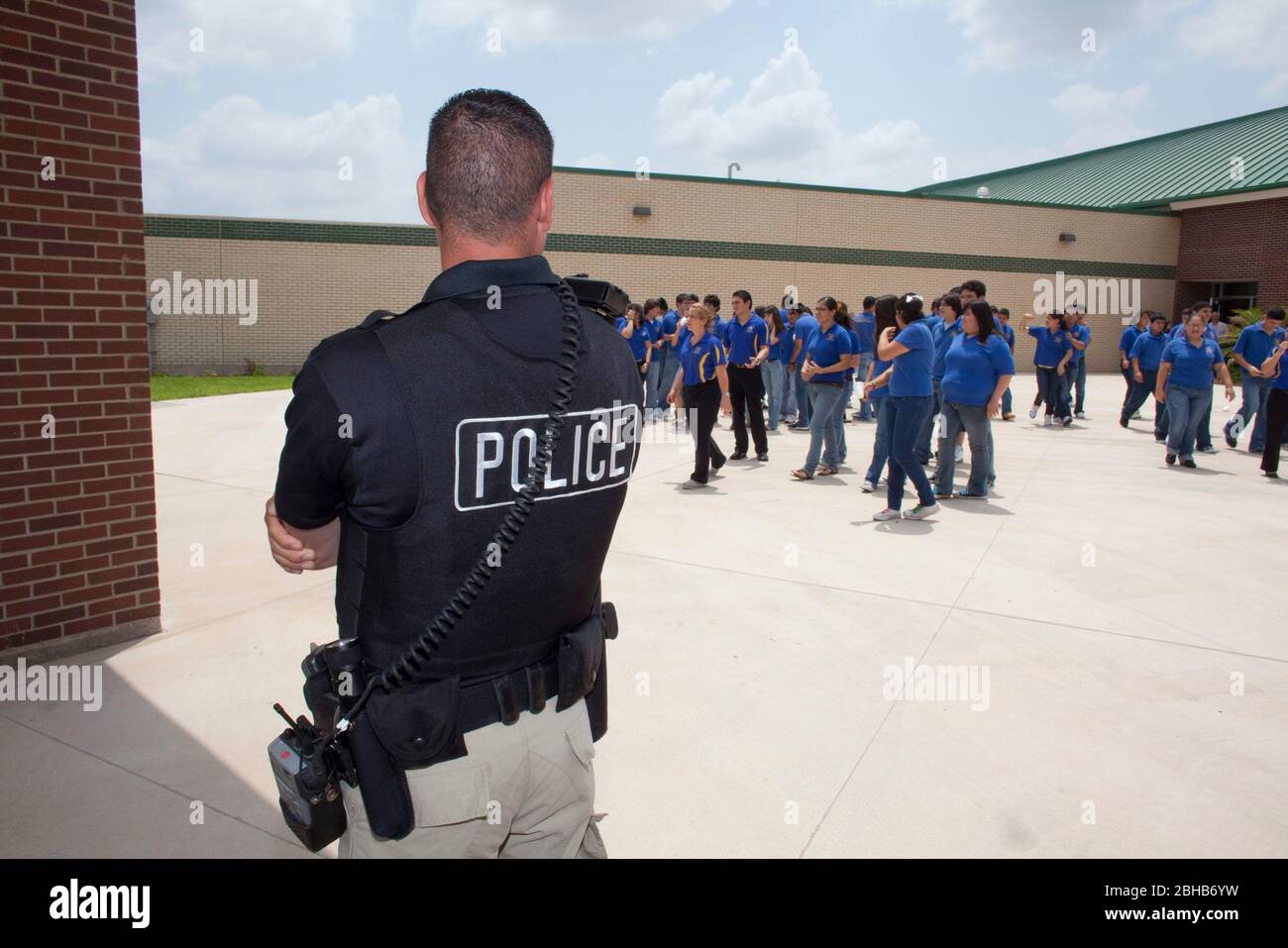 Pharr Texas USA, 13 maggio 2010: Gli studenti delle scuole superiori in attesa dei loro autobus scolastici sono sorvegliati dalla polizia locale che viene assegnata ai dettagli di sicurezza presso la scuola nel Texas estremo sud. Gli studenti devono indossare le magliette blu uniformi durante la giornata scolastica. ©Bob Daemmrich Foto Stock