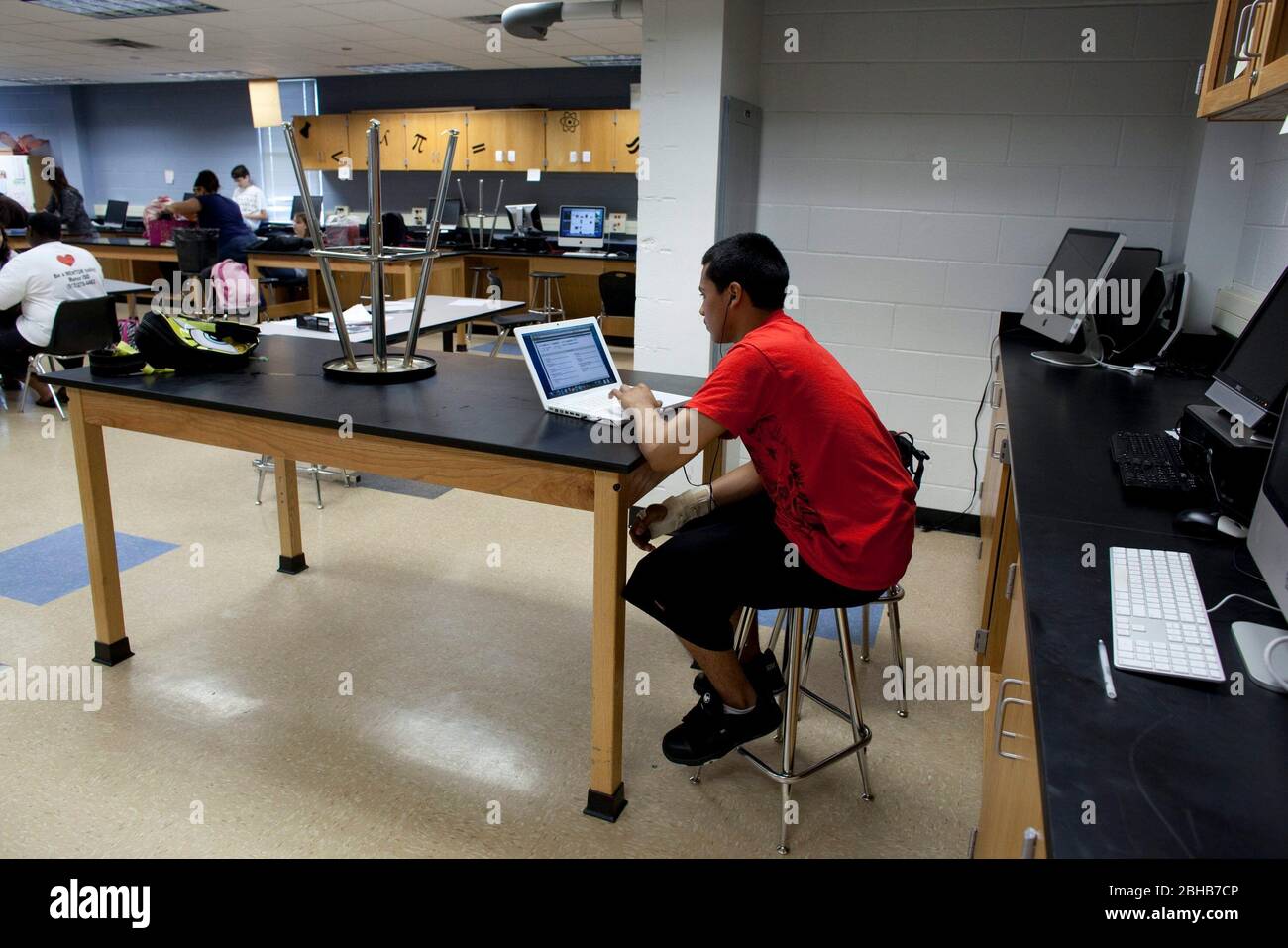 Manor Texas USA, maggio 12 2010: Studente ispanico maschile con la mano destra in un bretella tipi uno-mano sul portatile di fronte alla fila di computer desktop in classe al Manor New Tech High School, una scuola pubblica innovativa che si concentra su progetto di apprendimento in TSTEM (Technology Science Engineering Mathematics) curriculum. ©Bob Daemmrich Foto Stock