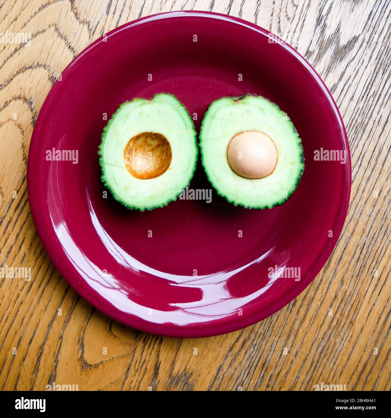 due metà di un avocado posto su una piastra rossa di ceramica che forma un volto felice Foto Stock