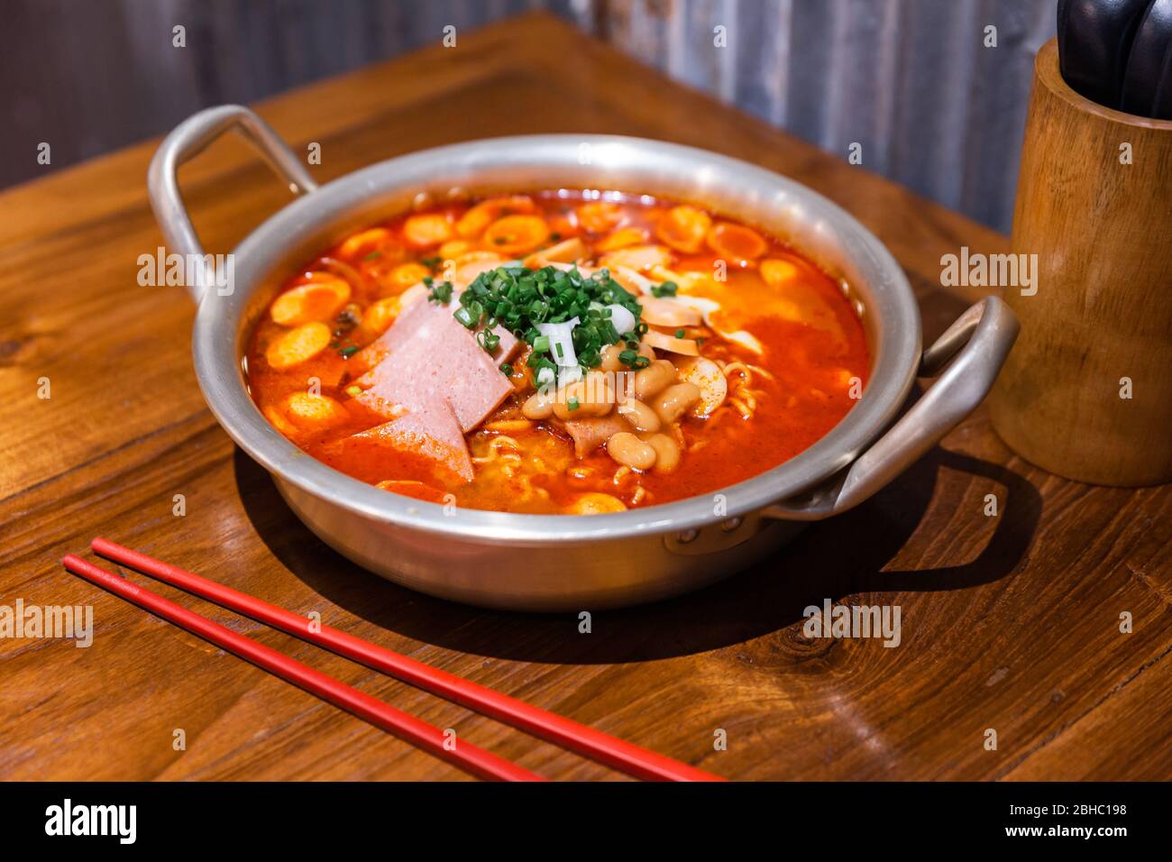 Zuppa tradizionale coreana di ramen con kimchi, prosciutto, salsiccia e formaggio in una ciotola d'argento su un tavolo di legno. Cucina coreana. Gustoso cibo asiatico. Foto Stock