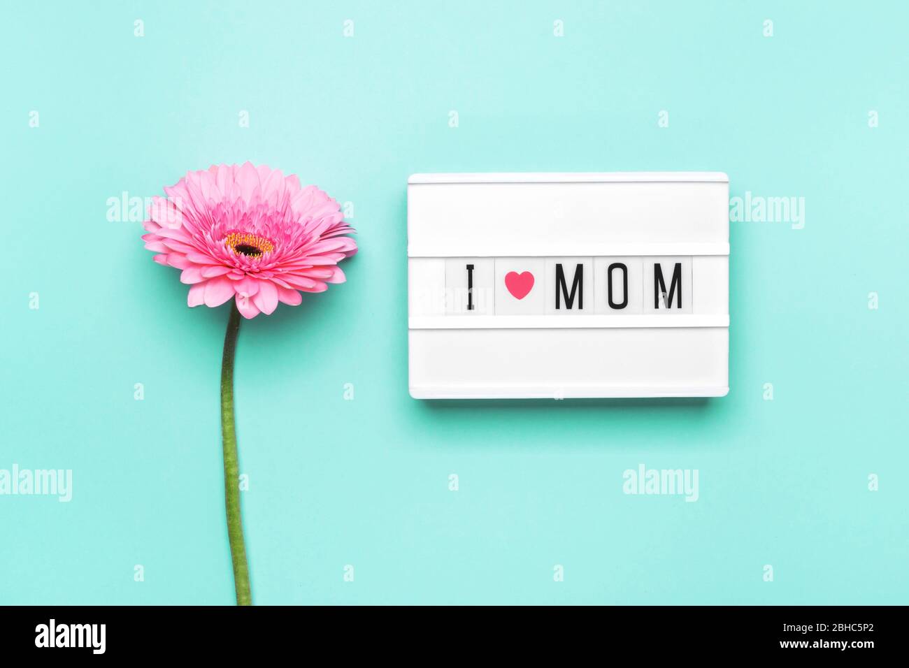 Amo il testo della mamma e il fiore di gerbera rosa su sfondo turchese. Sfondo su carta e scatola luminosa. Amo il concetto di mamma. Foto Stock