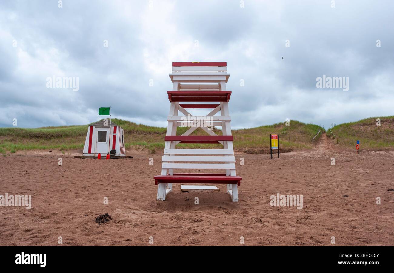 Stazione bagnino e sedia di osservazione sulla North rustico Beach. Bandiera verde di segnalazione calmo surf. Dune costali sotto un cielo sovrastato. PEI, Canada Foto Stock