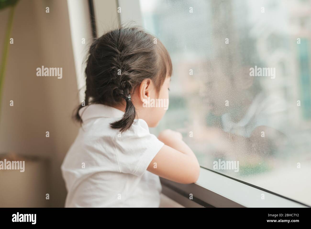 Vista posteriore a cute Little Girl guarda fuori dalla finestra Foto Stock