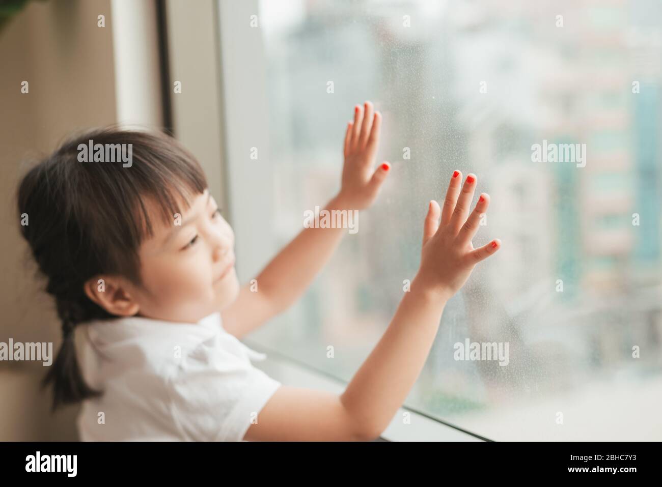 Bambina asiatica seduta a casa e guardando la finestra. Foto Stock