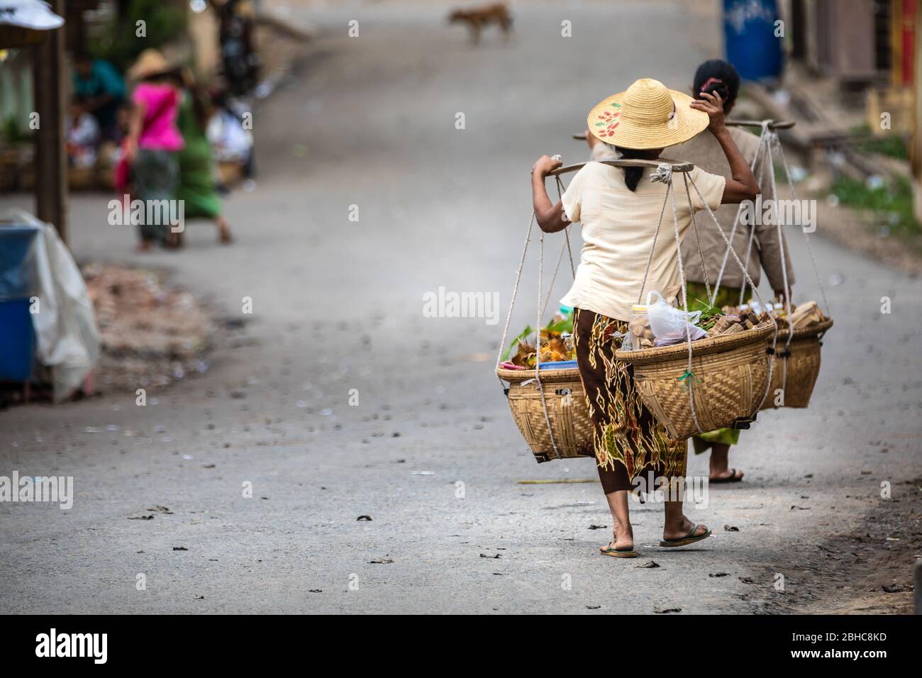 Donne birmane che trasportano il cibo con un metodo tipico. Abiti con caratteristico cappello del luogo. Sulla strada con spazio copia a sinistra. Posizione: Foto Stock