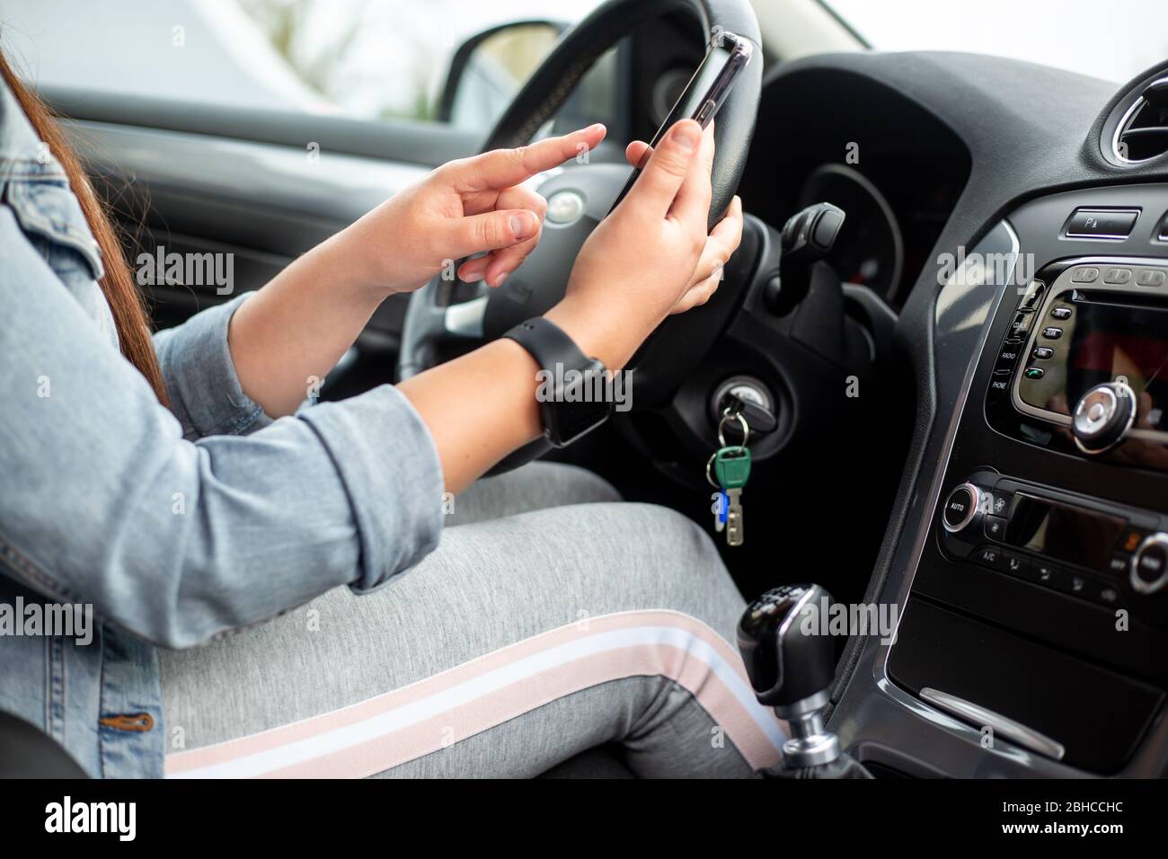 Donna conducente che utilizza un cellulare, smartphone durante la guida della sua auto, concetto pericoloso Foto Stock