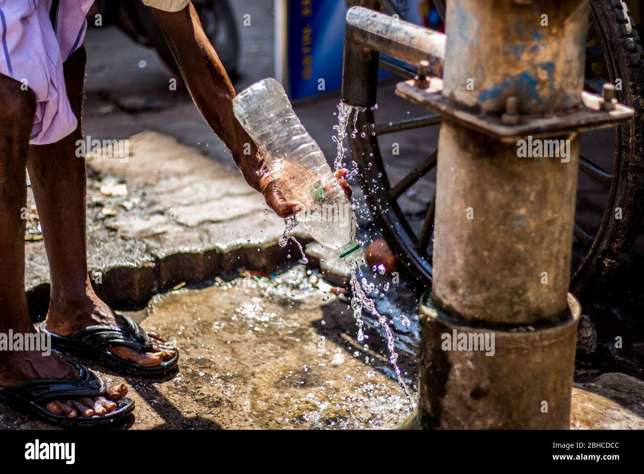 L'uomo che usa la bottiglia d'acqua le sue mani ad una pompa dell'acqua della mano nella campagna indiana. Uso della pompa dell'acqua manuale su strada. Pompa a mano per tirare sotto il suolo wat Foto Stock