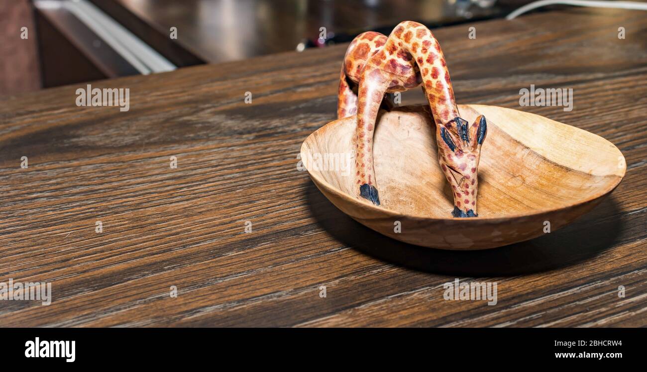 Piccola giraffa di legno mentre beve su un piatto di legno Foto Stock