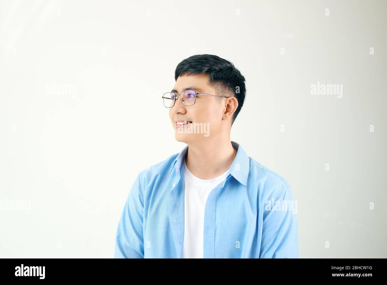 Giovane uomo che guarda lontano in piedi, indossando occhiali rotondi, isolato su bianco Foto Stock