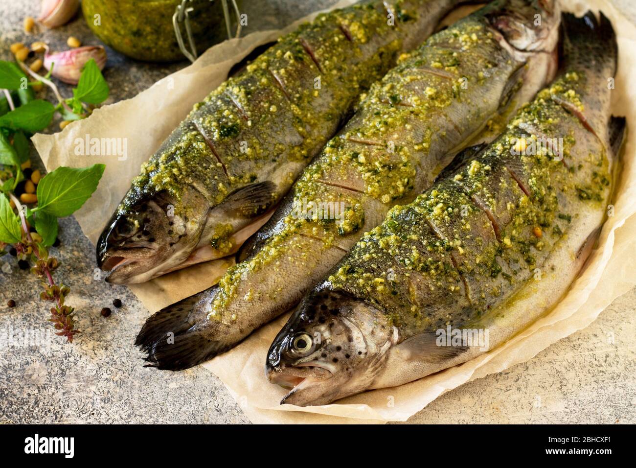 Cottura al salmone fresco. Pesce marinato con salsa di pesto e spezie culinarie su un piano in pietra grigia. Foto Stock