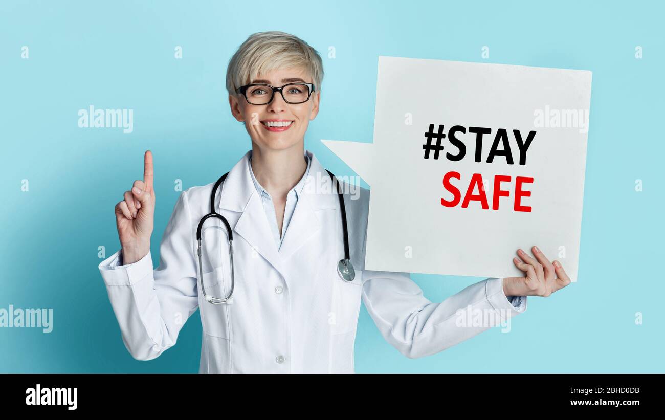 Medico femminile rivolto verso l'alto e tenendo bolla di discorso con hashtag RIMANERE SICURO su sfondo blu, collage Foto Stock