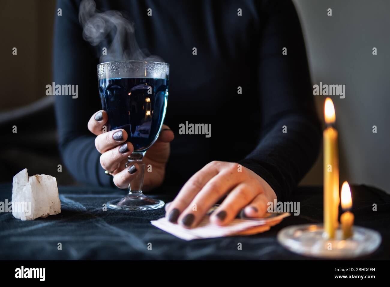 Le mani femminili che tengono la pozione magica di amore e le schede occultic di fortuna-dire su sfondo scuro. Foto Stock