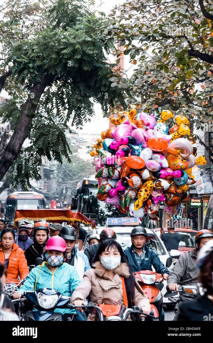 Hanoi, Vietnam, 30 dicembre 2019, piloti non identificati con e senza maschera, un venditore di balloni e alberi sullo sfondo, pochi giorni prima del Tet Foto Stock