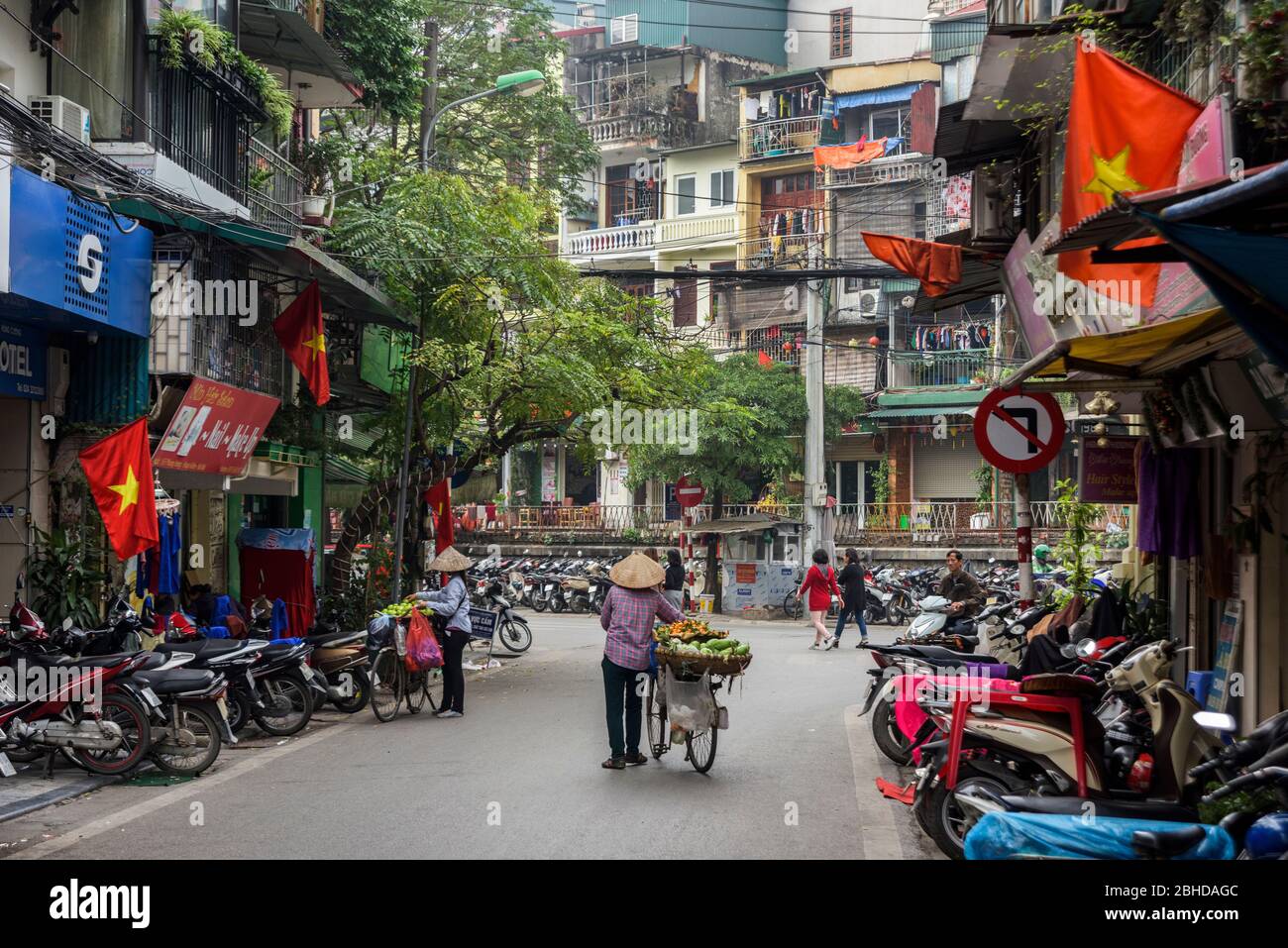 Hanoi, Vietnam, 30 dicembre 2019 - Vista posteriore su una vecchia signora, venditore di cibo di strada, spingendo la sua bicicletta piena di frutta in vendita, nel mezzo di una strada Foto Stock