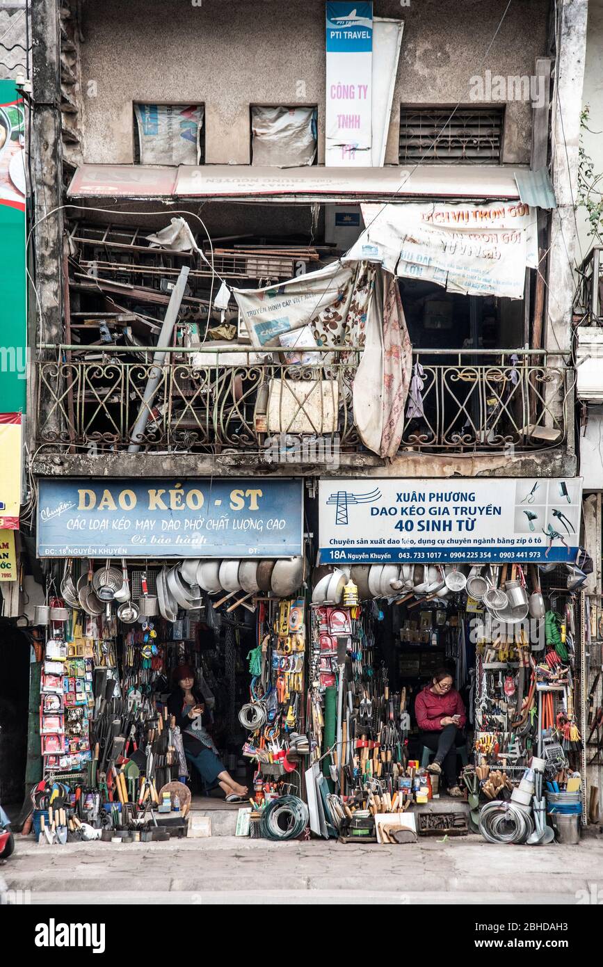 Hanoi, Vietnam, 30 dicembre 2019 - venditore che guarda il suo telefono cellulare mentre aspetta un cliente in un piccolo negozio di specialità per le strade di Han Foto Stock
