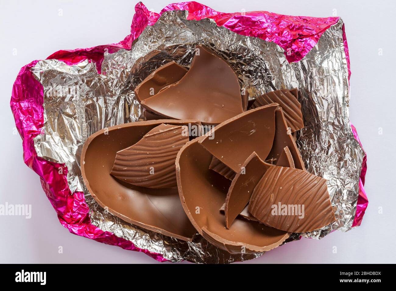 Cioccolato al latte uovo di Pasqua spezzato in pezzetti di lamina d'argento rosa isolato su sfondo bianco Foto Stock