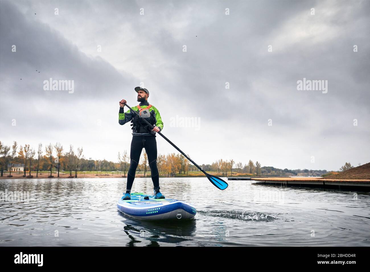 Atleta in neoprene paddleboard ad esplorare il lago a freddo contro il cielo nuvoloso Foto Stock