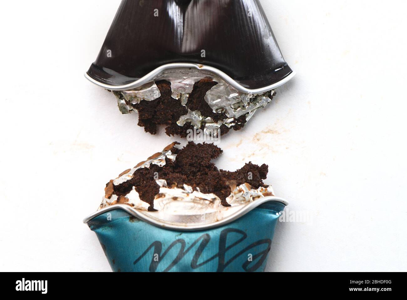 Un primo piano di una capsula Nespresso schiacciata in modo che il caffè venga estratto dal baccello di alluminio su uno sfondo bianco. Foto Stock