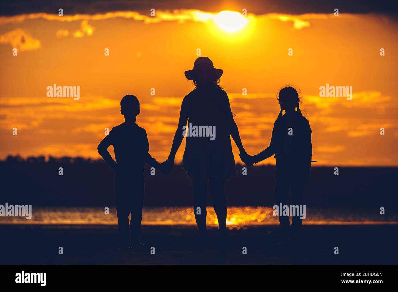 silhouette di mamma figlia e figlio su sfondo tramonto Foto Stock