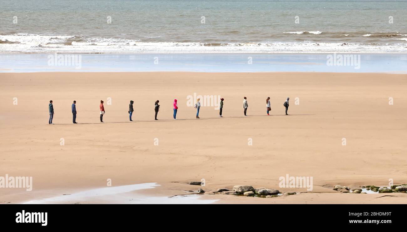 Le distanze sociali in una fila ordinata sulla spiaggia di Dunraven sulla costa del patrimonio di Glamorgan nel Regno Unito del Galles del Sud Foto Stock